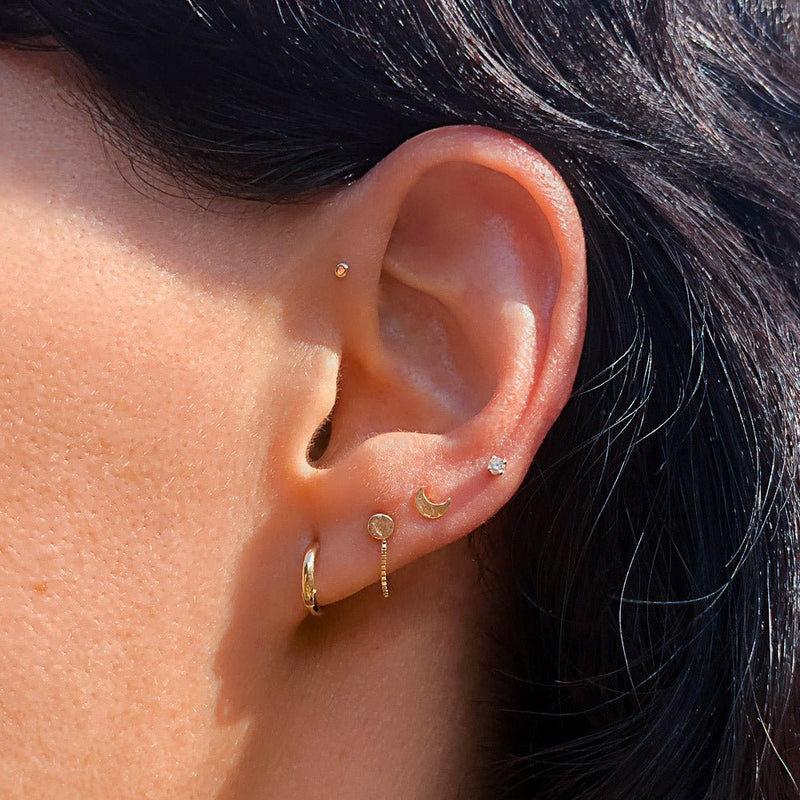 Gold box chain piercing connector on model's ear shown with hoop and gold moon stud styling