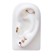 Gold diamond flower helix stud styled on white ear display among multiple gold cartilage piercings