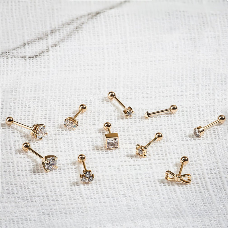 14k yellow gold diamond flower helix stud among assorted gold cartilage studs on white linen surface
