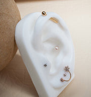14k gold industrial barbell displayed on white ear model prop alongside other gold ear piercings