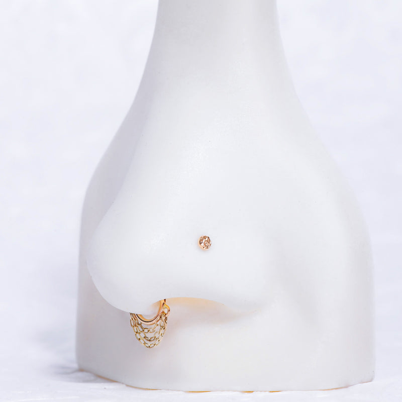 Tiny 14K gold hammered disc flat back shown in nose piercing on white display model for fit reference
