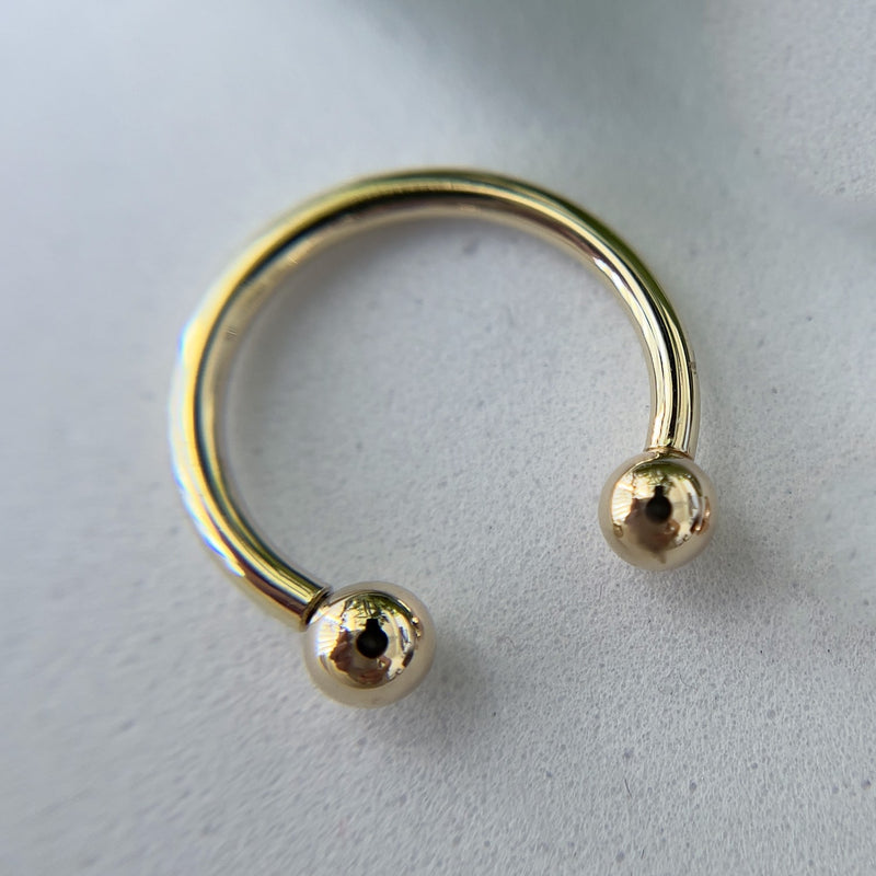 Close-up of 14k yellow gold horseshoe barbell showing mirror-polished finish and threaded ball ends