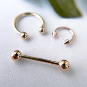 14k rose gold straight barbell styled with matching rose gold horseshoe rings on white surface