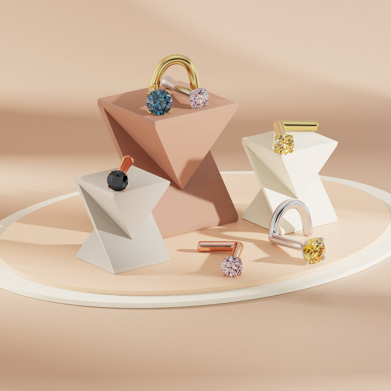 Assorted colored diamond prong nose studs displayed on geometric props in multiple gold tones