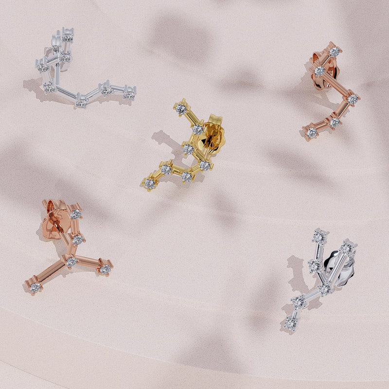Cancer constellation studs in yellow, rose, and white gold scattered on blush surface, showing front and back