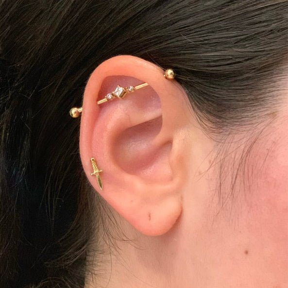 14K yellow gold triple CZ industrial barbell shown in a helix piercing on a model's ear