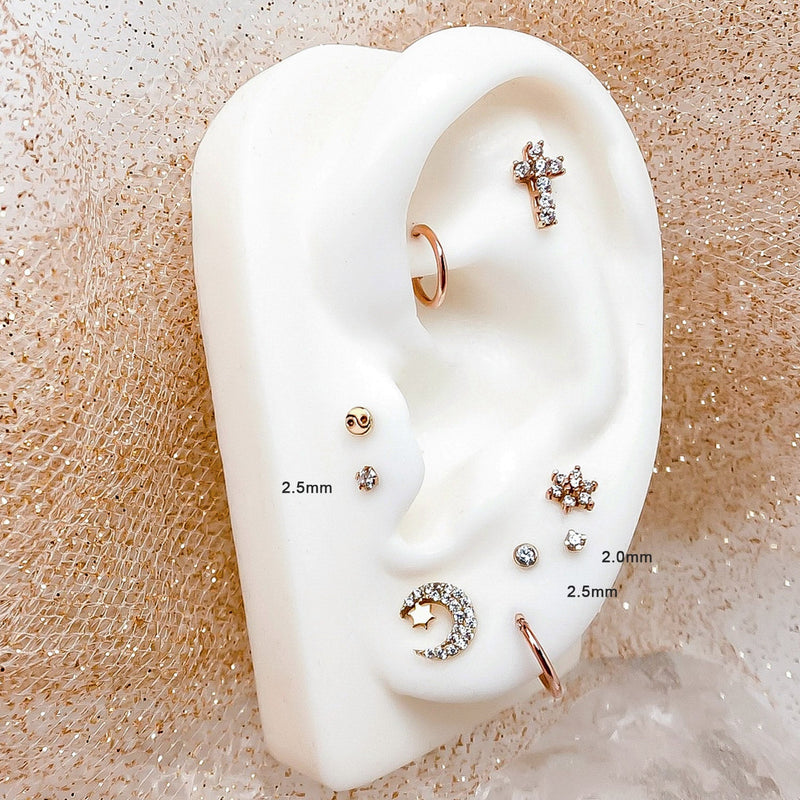 2.5mm diamond flat back stud labeled on silicone ear display alongside mixed rose gold piercing jewelry