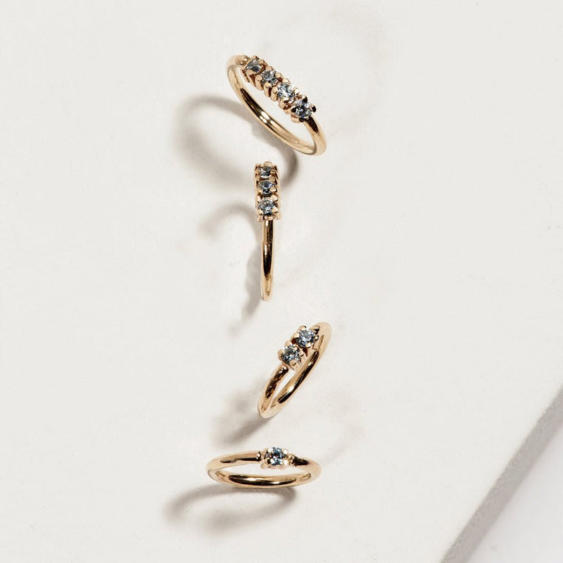 Four 14K yellow gold two-diamond seam ring hoops in multiple sizes arranged on white marble surface