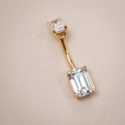 14k yellow gold double emerald-cut clear CZ navel ring laid flat on neutral surface, angled view