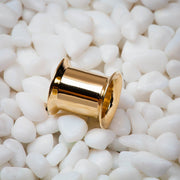 Single 14k yellow gold double flare ear tunnel resting on white pebbles, lifestyle close-up