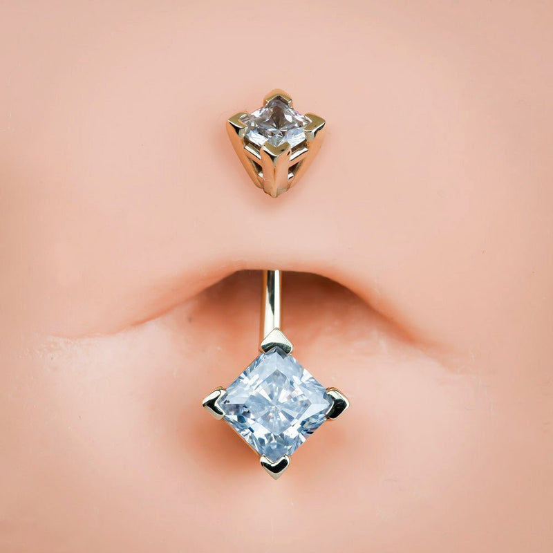 14k gold double princess-cut CZ belly ring shown in pierced navel with light blue lower gem