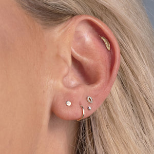 14K gold feather flat back earring worn in helix piercing, styled with multiple ear piercings on model
