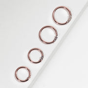 Four 14K rose gold diamond seam rings in graduated sizes arranged diagonally on white surface