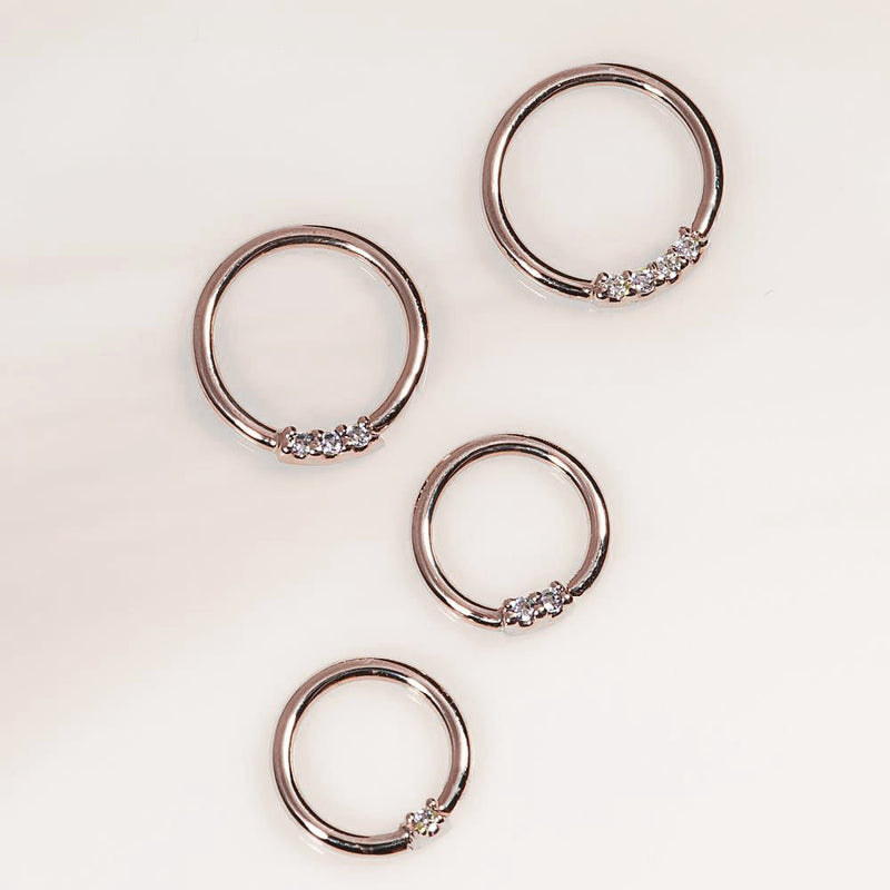 14K rose gold two-diamond seamless hoops in four sizes laid flat on light background