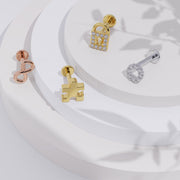 14K yellow gold puzzle piece flat back labret displayed on tiered white surface with other gold charm earrings
