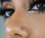 Purple CZ flower 14K gold nose bone shown in pierced nostril on model for fit and scale reference
