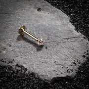 14k rose gold CZ prong flat back labret resting on dark stone surface, editorial lifestyle shot