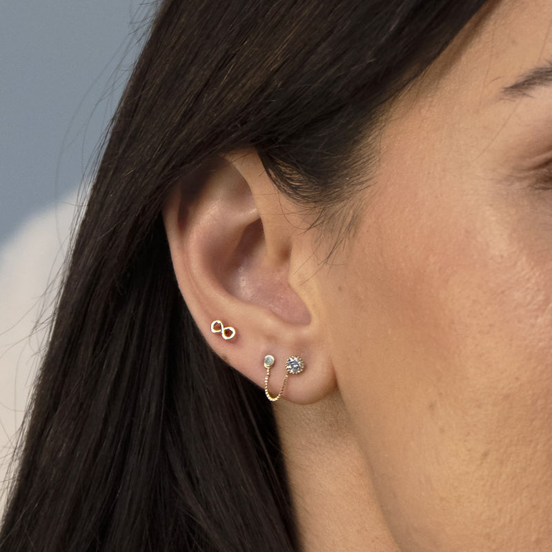 14K gold infinity flat back earring worn in lobe piercing, styled with chain earring on model