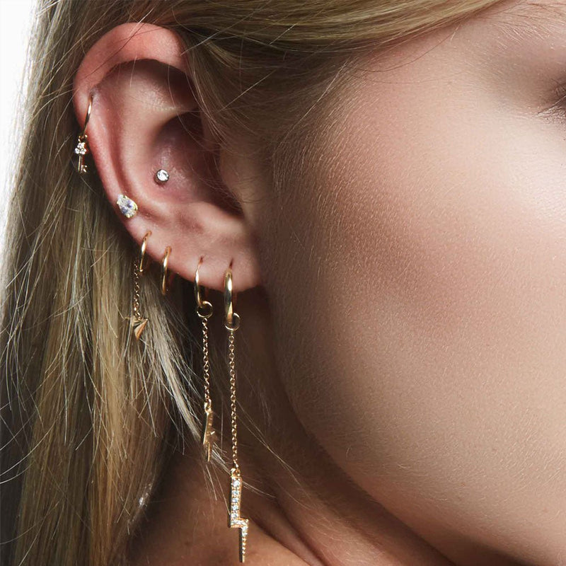 Pear diamond 14k gold flat back stud in helix piercing styled with gold hoops and chain earrings on model