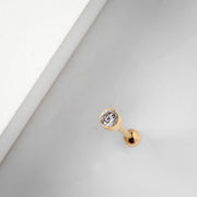 14k yellow gold 3mm bezel CZ cartilage earring resting on white surface, lifestyle close-up