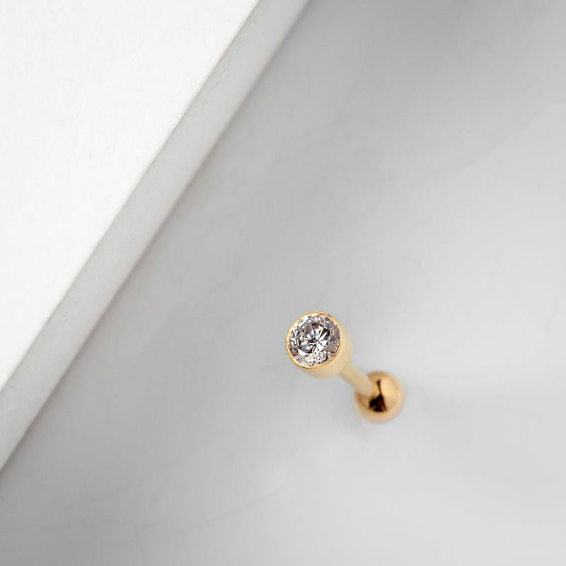 14k yellow gold 3mm bezel CZ cartilage earring resting on white surface, lifestyle close-up