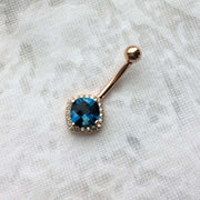 14k rose gold London blue topaz diamond halo navel ring laid on fabric for scale and texture detail