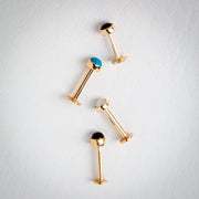 Four yellow gold flat back labret studs with cabochon tops laid flat, including opal, turquoise, and onyx options