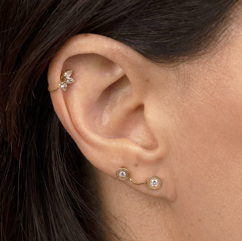 Gold box chain connector linking helix CZ stud and two bezel CZ lobe studs on model's ear