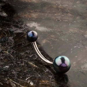 Peacock pearl 14k gold navel ring resting on dark stone surface, showing blue-green iridescence