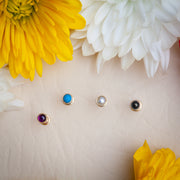 Four 3mm gold bezel cabochon ends — amethyst, turquoise, pearl, and onyx — displayed flat near flowers