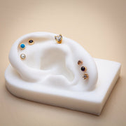 Pearl cabochon flat back stud on white ear mold alongside turquoise, onyx, and CZ gold studs