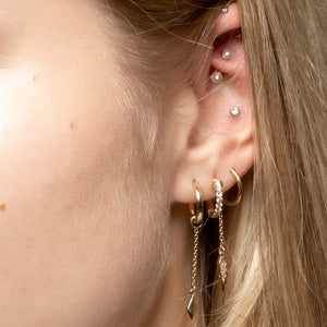 Pearl bezel-set curved barbell worn in rook piercing, styled with gold ear stack