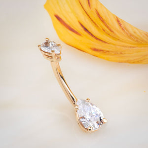 14k yellow gold pear CZ navel ring shown at an angle beside a flower petal for scale