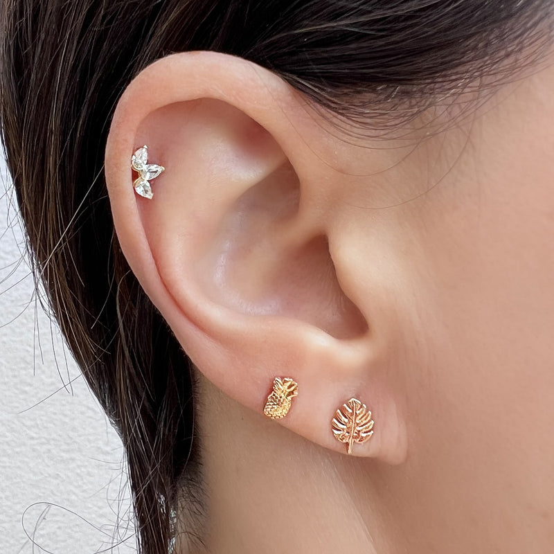 14K rose gold monstera leaf flat back earring worn in lobe piercing, styled with gold pineapple and CZ cartilage studs