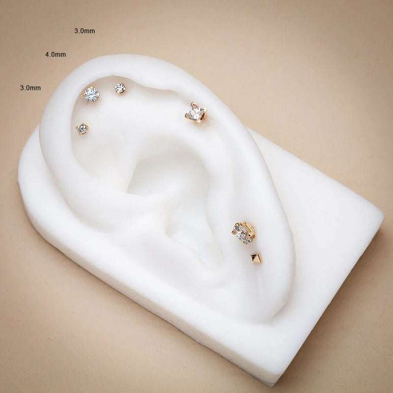 14k gold CZ flat back studs in 3mm and 4mm sizes displayed on white silicone ear model for size comparison