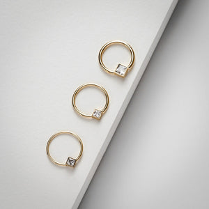 Three 14k yellow gold princess CZ fixed bead rings in graduated sizes on neutral surface