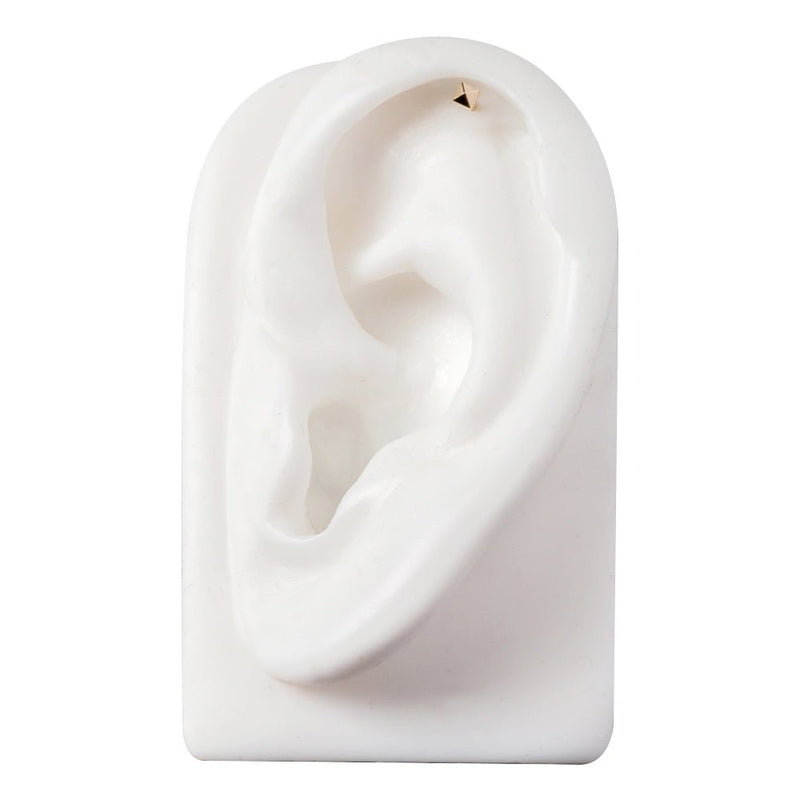 14k gold pyramid cartilage stud shown in helix piercing on white ear model, front-facing placement