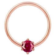 Close-up front view of 14k rose gold captive bead ring with faceted red CZ prong detail