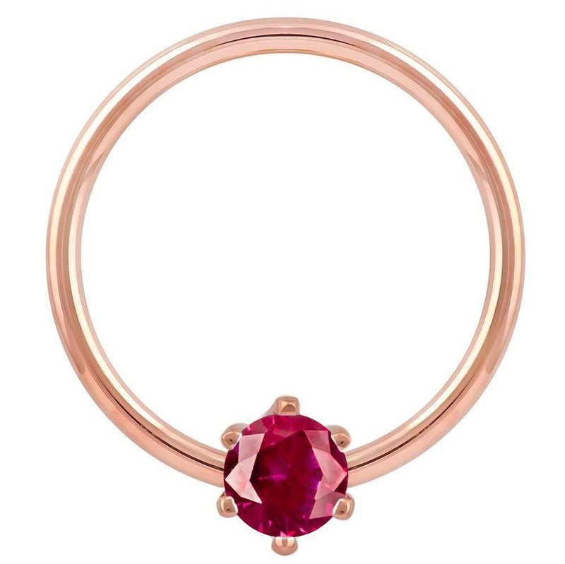 Close-up front view of 14k rose gold captive bead ring with faceted red CZ prong detail