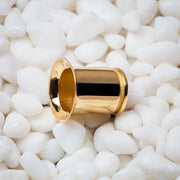 Single 14k yellow gold flare tunnel plug resting on white pebbles, angled close-up view