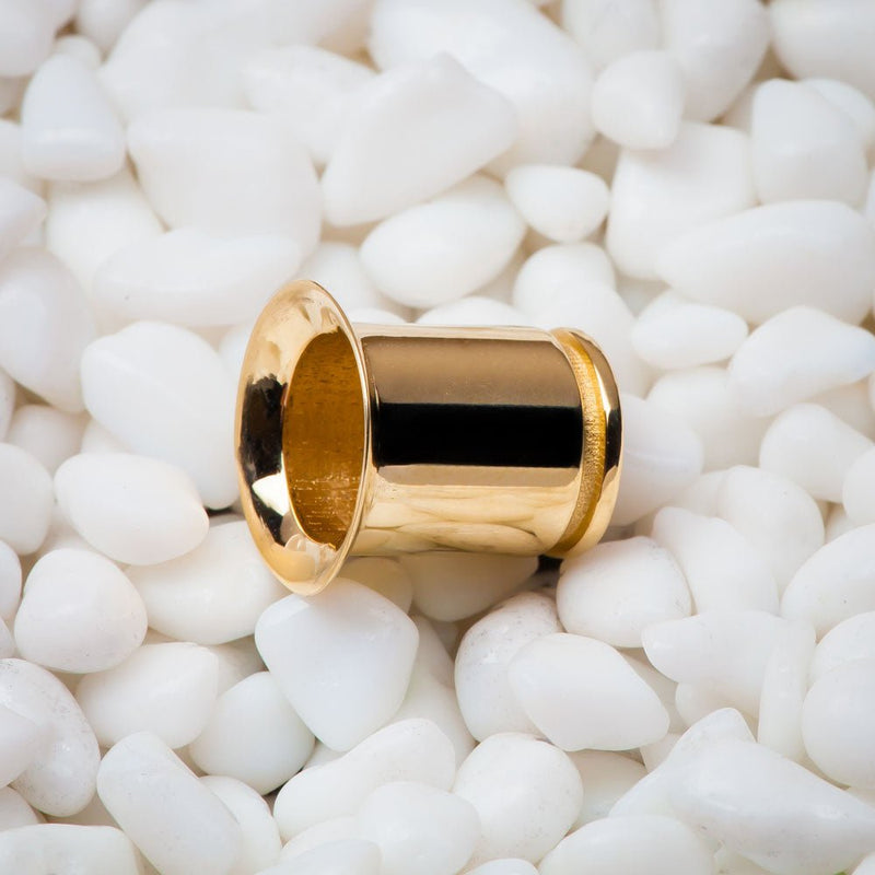 Single 14k yellow gold flare tunnel plug resting on white pebbles, angled close-up view