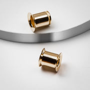 Pair of 14k yellow gold single flare ear tunnels on minimalist surface, styled flat lay