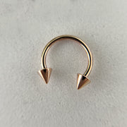 14K rose gold spike horseshoe barbell laid flat on stone surface, top-down view