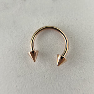 14K rose gold spike horseshoe barbell laid flat on stone surface, top-down view