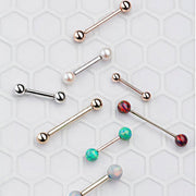 Assorted 14k gold straight barbells in rose gold, white gold, and yellow gold with opal and pearl ends displayed on tile