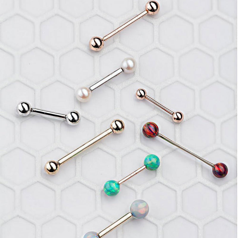 Assorted 14k gold straight barbells in rose gold, white gold, and yellow gold with opal and pearl ends displayed on tile