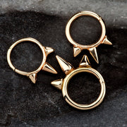 Three 14K rose gold triple spike seam rings in varying sizes shown on dark stone surface